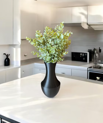 Matte black 3D printed vase with soft curved silhouette holding eucalyptus in a contemporary white kitchen.
