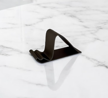Black minimal 3D printed phone stand with sculptural curved design on a marble surface.