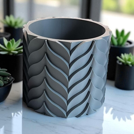 Gray 3D printed planter with raised leaf-pattern sculptural design surrounded by succulents.